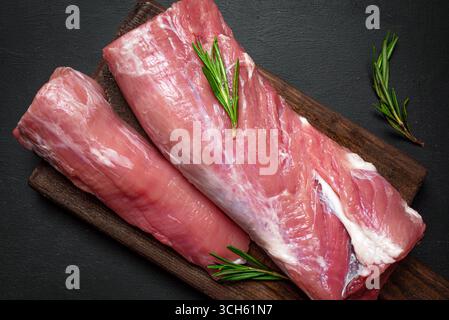 Viande de filet de porc non cuite prête à cuire sur fond de bois avec romarin, vue de dessus. Morceaux de viande juteuse fraîche en gros plan. Banque D'Images