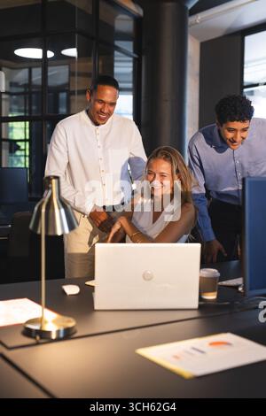 Collègues collaborant sur ordinateur portable dans un bureau moderne, souriant et discutant du projet Banque D'Images