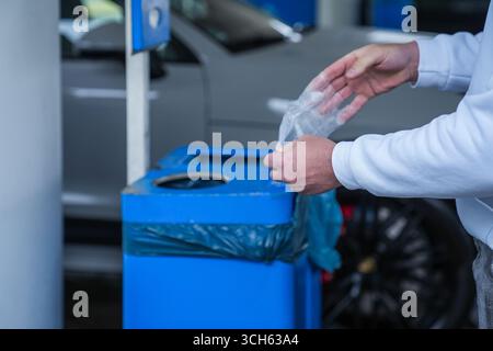 Homme jetant un gant jetable dans la poubelle d'une station-service Banque D'Images