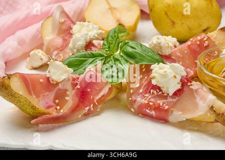 Tranche de poire enveloppée dans du prosciutto avec du fromage et des graines de sésame sur un tableau blanc Banque D'Images