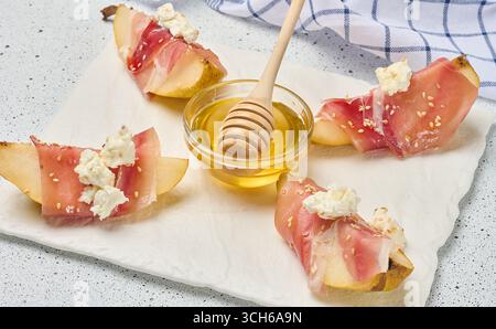 Tranche de poire enveloppée dans du prosciutto avec du fromage et des graines de sésame sur un tableau blanc Banque D'Images
