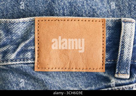 Tissu jeans avec étiquette en cuir gros plan. Fond de texture denim. Détail vêtements de mode avec écusson marron. Concept moderne de l'industrie textile. Banque D'Images