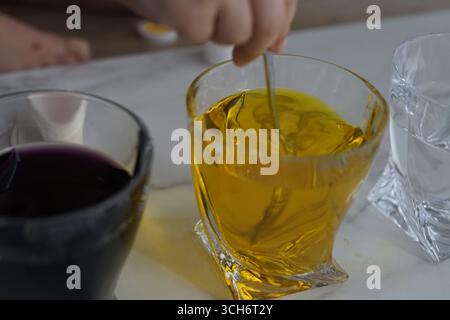Une scène vibrante avec une main remuant un liquide jaune dans un verre. Les verres environnants contiennent des liquides violets et clairs, créant un visuel attrayant Banque D'Images