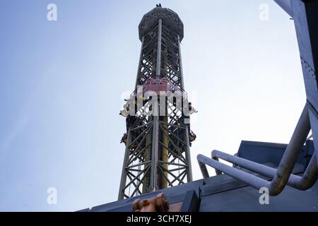 Une grande tour de parc d'attractions transporte les coureurs sur une descente verticale sous un ciel bleu vif Banque D'Images
