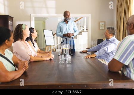 Homme principal dirigeant la réunion avec un groupe diversifié à la maison, discutant des plans. Travail d'équipe, leadership, brainstorming, stratégie, collaboration, réunion d'affaires Banque D'Images