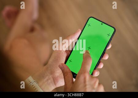 Mains tenant le smartphone et l'écran tactile avec écran vert et marqueurs de suivi. Personne utilisant un téléphone portable, gros plan Banque D'Images