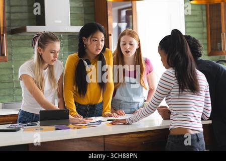 Collaboration sur un projet scolaire dans la cuisine, amis adolescents discutant des idées avec enthousiasme Banque D'Images
