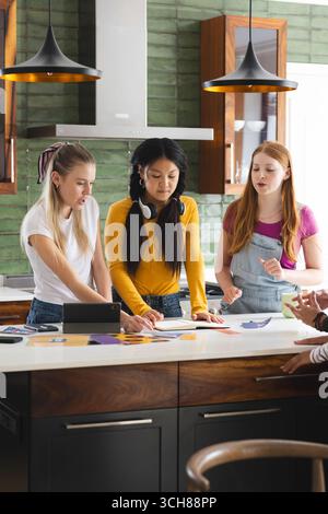 Adolescentes collaborant sur un projet scolaire dans une cuisine moderne, discutant des idées Banque D'Images