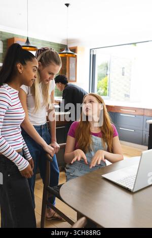 Adolescentes collaborant sur un projet scolaire en utilisant un ordinateur portable dans un cadre de cuisine Banque D'Images