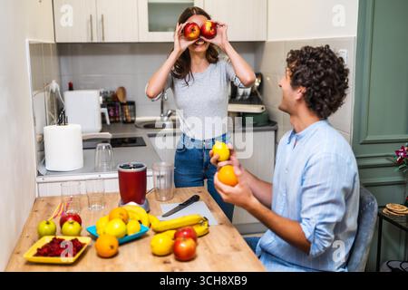 Un jeune couple joyeux fait un smoothie aux fruits frais dans leur cuisine à la maison, profitant d'une alimentation saine et de la vie domestique. Banque D'Images