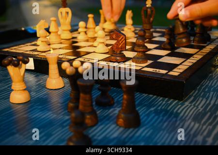 Mains déplaçant des pièces d'échecs sur échiquier en bois lors d'un jeu en extérieur avec quelques pièces posées sur la table. Banque D'Images