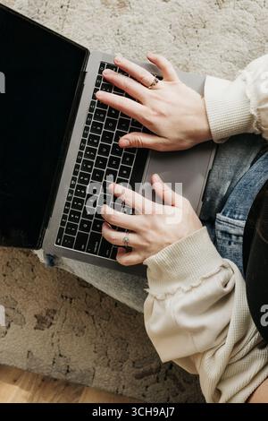 Femme d'âge moyen s'assoit sur le sol tout en travaillant sur un ordinateur portable Banque D'Images