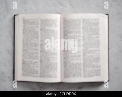Livre ouvert flou couché sur une table montrant un texte flou, fond parfait pour l'éducation ou les concepts de religion Banque D'Images