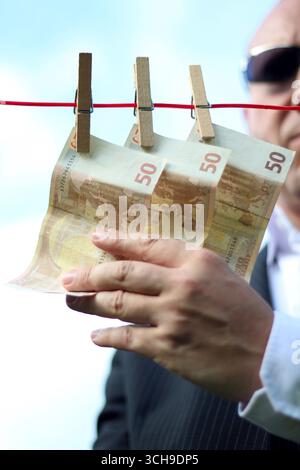 un sinistre gars attrape l'argent qui est accroché à une corde à linge, utilisable pour les crises de l'euro, le blanchiment d'argent, les crises financières etc Banque D'Images