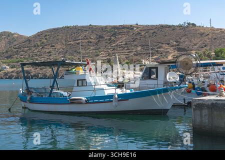 Bateaux de pêche blancs et bleus amarrés dans le port de Pomos, Chypre, par une journée ensoleillée avec des collines en arrière-plan Banque D'Images