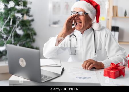 Médecin âgé senior dans le chapeau de Santa sur le quart de la veille de noël tenant l'annonce criante de la main. copier l'allure Banque D'Images
