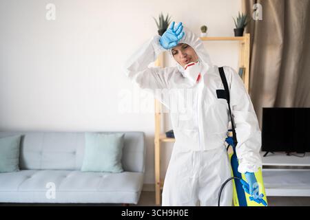 Exterminateur féminin fatigué surchargé du service de lutte antiparasitaire travaillant à l'intérieur de la maison avec bouteille de pulvérisateur à la maison. Copier l'espace Banque D'Images
