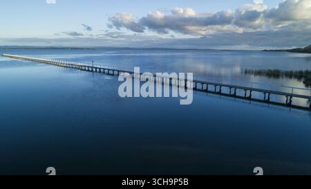 Vue aérienne de la longue jetée s'étendant loin dans les eaux bleues chatoyantes sous un ciel serein, Lakes Entrance, Victoria, Australie. Banque D'Images