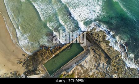 Vue aérienne des vagues mousseuses qui s'écrasent contre la côte accidentée, contrastant avec la piscine calme et rectangulaire de l'océan, North Narrabeen, Nouvelle-Galles du Sud, Australie. Banque D'Images