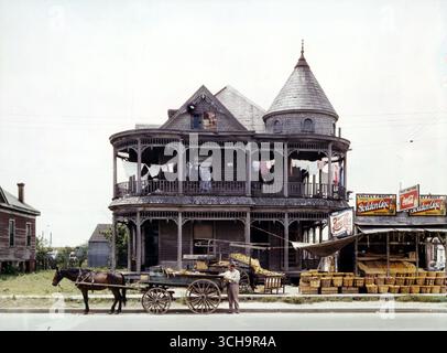 House in Houston, Texas, mai 1943. Photographie couleur FSA par John Vachon. Montre maison en bois de style victorien, buanderie suspendue à la galerie supérieure ; en face est un chariot tiré par un cheval. À droite de la photo se trouve un stand de fruits et des panneaux publicitaires Banque D'Images