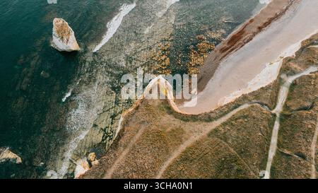 Un rivage rocheux avec une falaise et une petite formation rocheuse. L'eau est calme et le ciel dégagé Banque D'Images