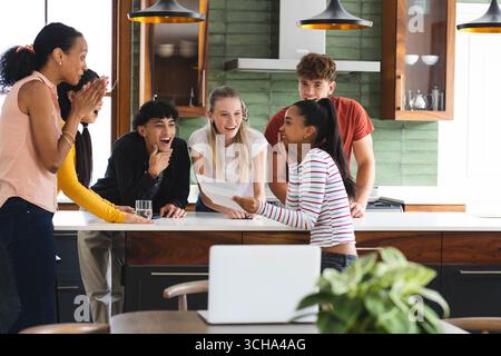 Adolescents divers célébrant dans la cuisine, partageant des nouvelles passionnantes et appréciant la vie commune, à la maison. Célébration, bonheur, amitié, liaison, fête, yo Banque D'Images