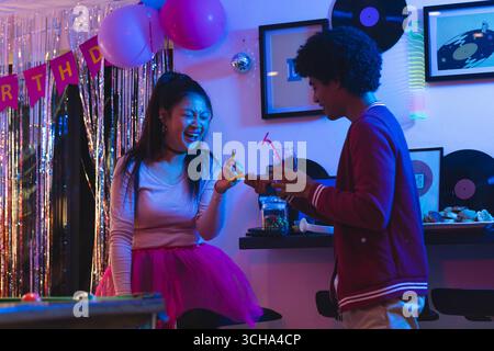 Adolescents divers amis appréciant la fête d'anniversaire avec des boissons et des rires dans la salle de fête, à la maison. Célébration, boissons, amitié, à l'intérieur, rassemblement Banque D'Images