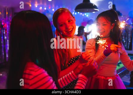 Divers amis adolescents célébrant avec des pétillants à la fête, profitant d'une atmosphère festive, à la maison. célébration, amitié, excitation, nuit, vacances Banque D'Images