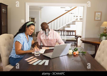 Couple senior afro-américain diversifié planifiant la rénovation de la maison en utilisant un ordinateur portable à la table à manger. Amélioration de la maison, technologie, travail d'équipe, brainstorming, l Banque D'Images