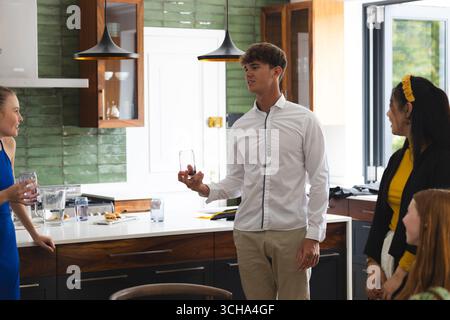 Amis adolescents appréciant la conversation et les boissons dans la cuisine moderne pendant la célébration. Amitié, fête, boissons, bavardage, rassemblement Banque D'Images