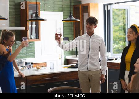 Amis adolescents célébrant à la maison, levant des verres et souriant dans la cuisine. célébration, toast, salon, bonheur, socialisation, ensemble Banque D'Images