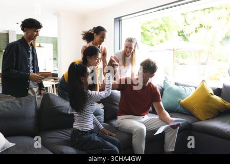 Des amis adolescents célébrant le succès à la maison, des hauts-fours et souriants sur le canapé. Célébration, amitié, bonheur, accomplissement, joie, jeunesse Banque D'Images