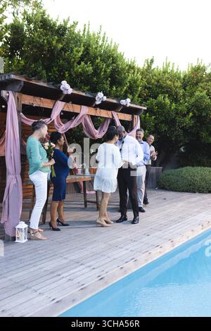 Au mariage, célébrant au bord de la piscine, divers amis seniors appréciant dans le jardin se réunissant avec le sourire. senior divers amis, fête, célébration, happ Banque D'Images