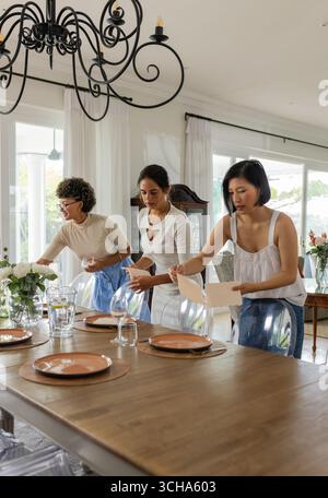 Disposer des assiettes et des verres, les femmes mettant une table à manger élégante pour la célébration, à la maison. vaisselle, festive, décorations, hospitalité, préparation Banque D'Images