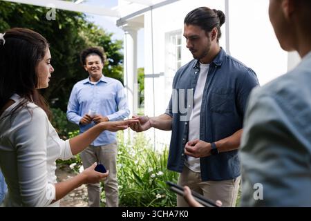 Échanger des anneaux à l'extérieur, couple célébrant l'engagement avec des amis dans le jardin. Mariage, célébration, amour, relation, bonheur, amitié Banque D'Images