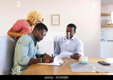 Amis examinant des documents ensemble à la maison, discutant des plans autour d'un café. Collaboration, travail d'équipe, discussion, planification, amitié, brainstorming Banque D'Images