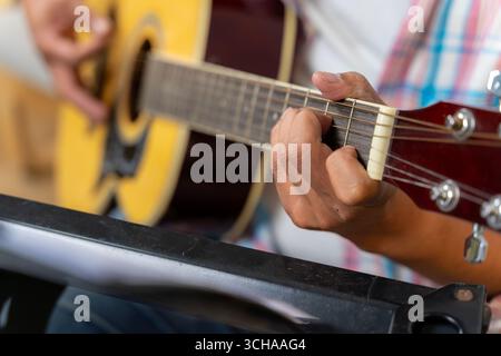 Une vue rapprochée d'une main pressant des accords sur une touche de guitare acoustique, mettant en évidence les cordes et les doigts dans le focus. Banque D'Images