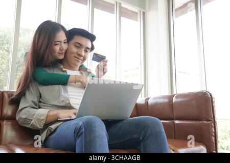 Un jeune couple magasinant en ligne à la maison ensemble, en utilisant une carte de crédit pour les achats, illustrant le commerce électronique moderne, la commodité et le style de vie Banque D'Images