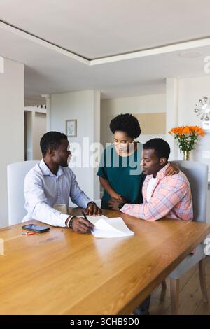 Examen de la paperasse financière couple afro-américain avec conseiller à la table à manger, avec tasse à café. Collaboration, professionnel, consultation, moderne Banque D'Images