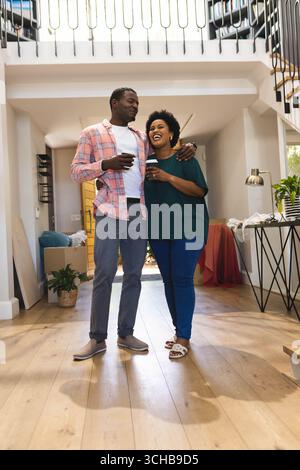 Tenant des tasses de café à emporter couple afro-américain s'installant dans l'entrée de la maison, avec des boîtes mobiles. Moderne, style de vie, confortable, design, maison, relaxation Banque D'Images