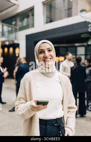 Portrait d'une femme professionnelle confiante portant le hijab tenant le téléphone intelligent dans le centre de congrès Banque D'Images