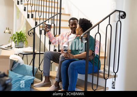 Couple assis dans les escaliers, appréciant le café et prenant selfie à la maison. Ensemble, loisirs, technologie, détente, style de vie, collage Banque D'Images