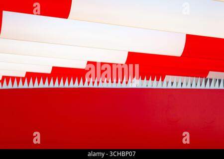 Dents pointues triangulaires blanches dépassant dans une rangée du rouge, sur un fond rayé rouge et blanc. Banque D'Images