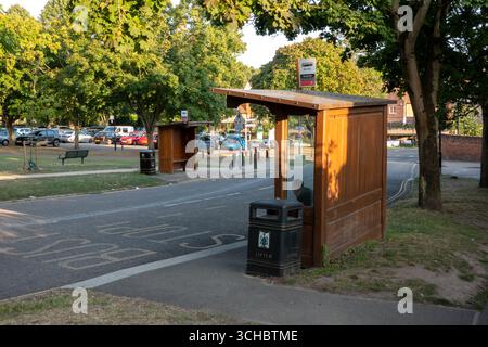 Une scène de rue à Saffron Walden, Essex, avec un abri de bus en bois à un arrêt de bus en face d'un autre arrêt de bus avec des arbres environnants et une route. Banque D'Images