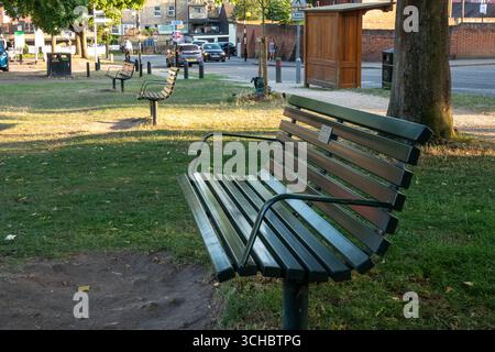 Banc en bois dans un parc à Saffron Walden, Essex, Angleterre. Arbres, rue, et un abri de bus wwoden en arrière-plan. Banque D'Images