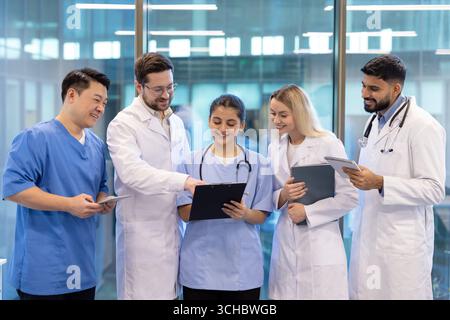 Les médecins et les infirmières examinent les dossiers médicaux, partagent leur expertise et collaborent aux soins aux patients dans un milieu hospitalier moderne, favorisant ainsi le travail d'équipe Banque D'Images