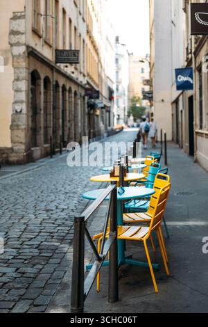 Chaises de café colorées jaunes et bleues et tables sur une rue pavée dans une ville européenne calme. Résilience urbaine, culture des petites entreprises, café Banque D'Images