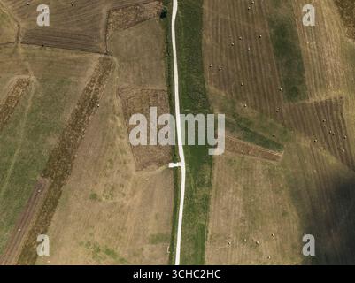 Vue aérienne d'une route blanche dure coupe un patchwork de champs terreux, créant un contraste frappant dans le paysage rural, Pescocostanzo, Abruzzes, Italie. Banque D'Images