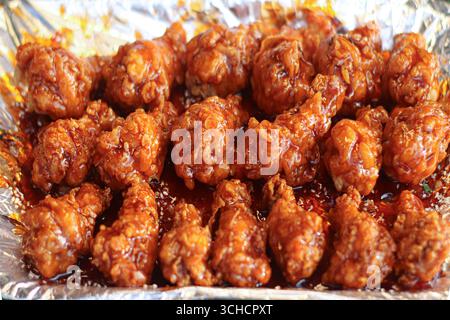 Ailes de poulet frites au caramel épicé thaïlandais sur plateau en aluminium, brun doré et brillant avec glaçage épicé sucré, scène asiatique authentique de Street food. Banque D'Images