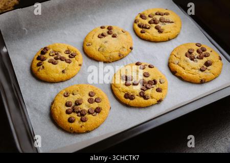 Biscuits aux pépites de chocolat fraîchement cuits dans un plateau sur du papier parchemin, gros plan sur la photographie alimentaire Banque D'Images